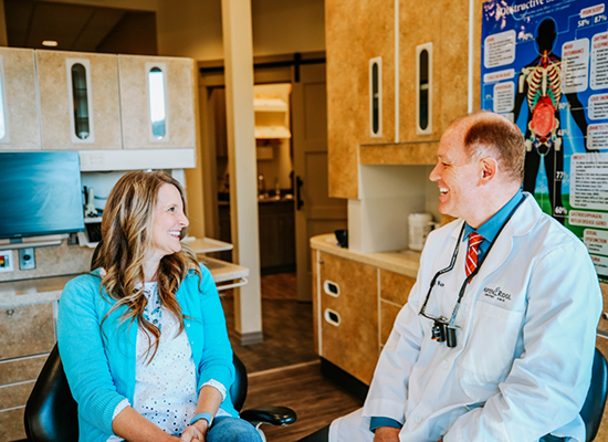 Male dentist in Colorado Springs talking to blonde female patient in dental chair