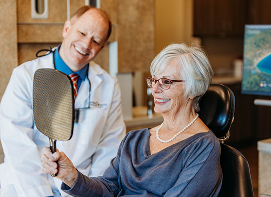 Female patient checking smile while biomimetic dentist in Colorado Springs looks on