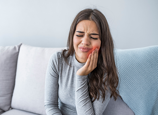 Woman with toothache sitting on couch needing emergency dentist in Colorado Springs